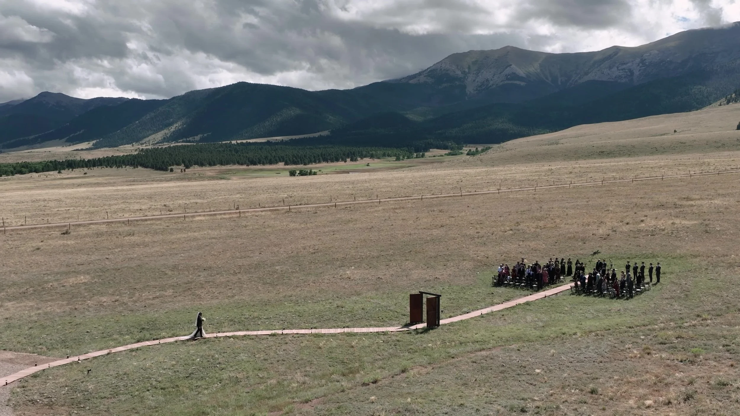 High-angle view of the outdoor ceremony at 3 Peaks Ranch in Westcliffe, Colorado, barn doors in the meadow under the mountains