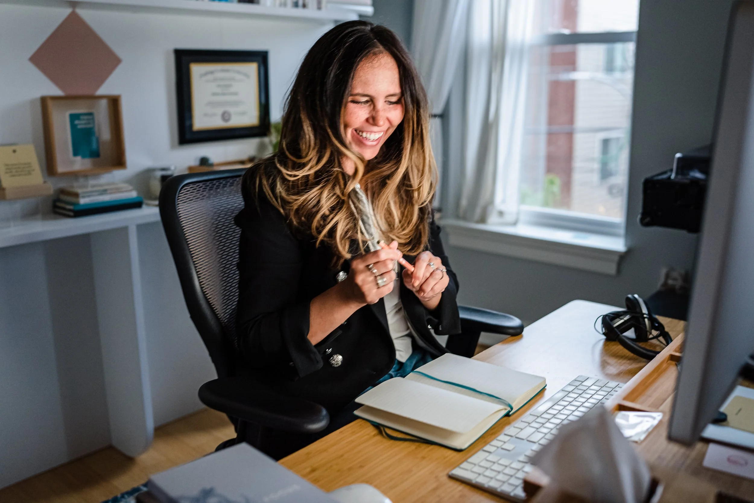 Coral Edwards laughing at her desk in her home office, mid-conversation