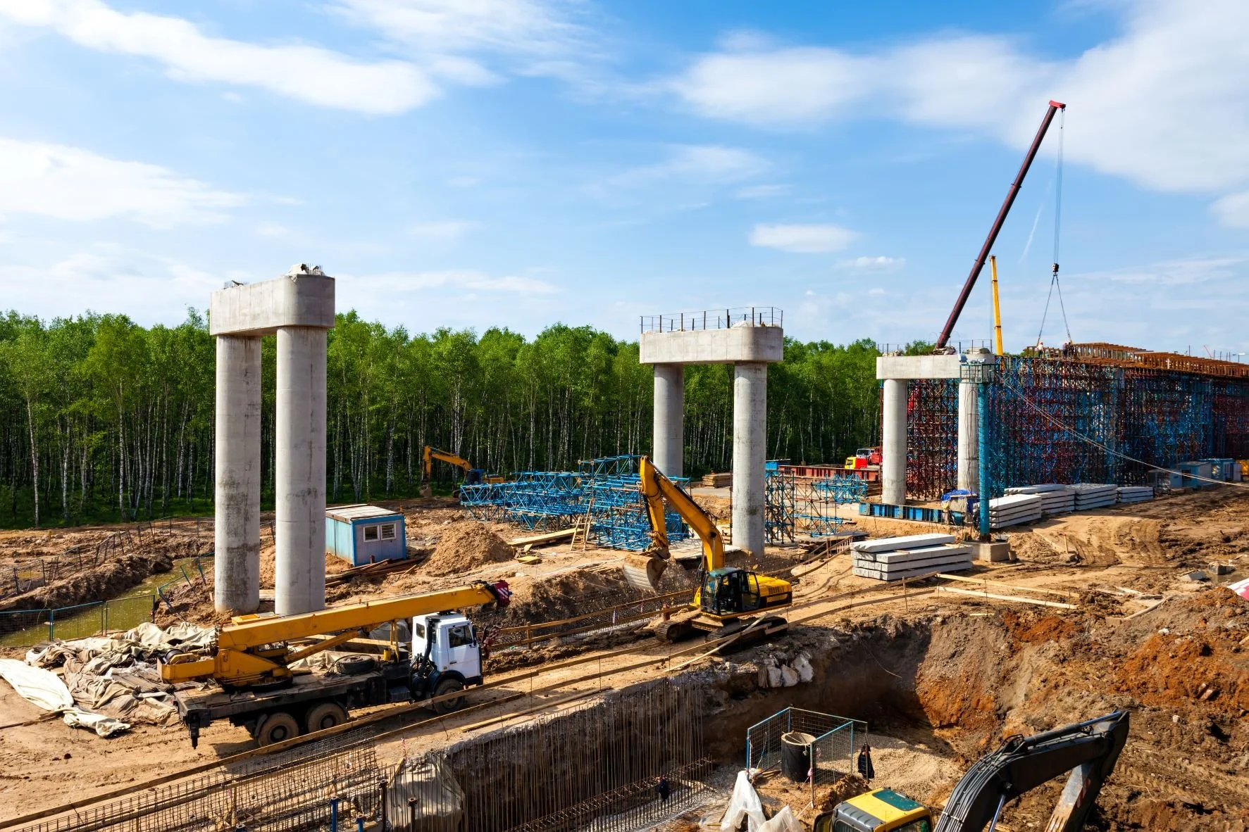 Cranes and excavators building concrete bridge supports on a construction site
