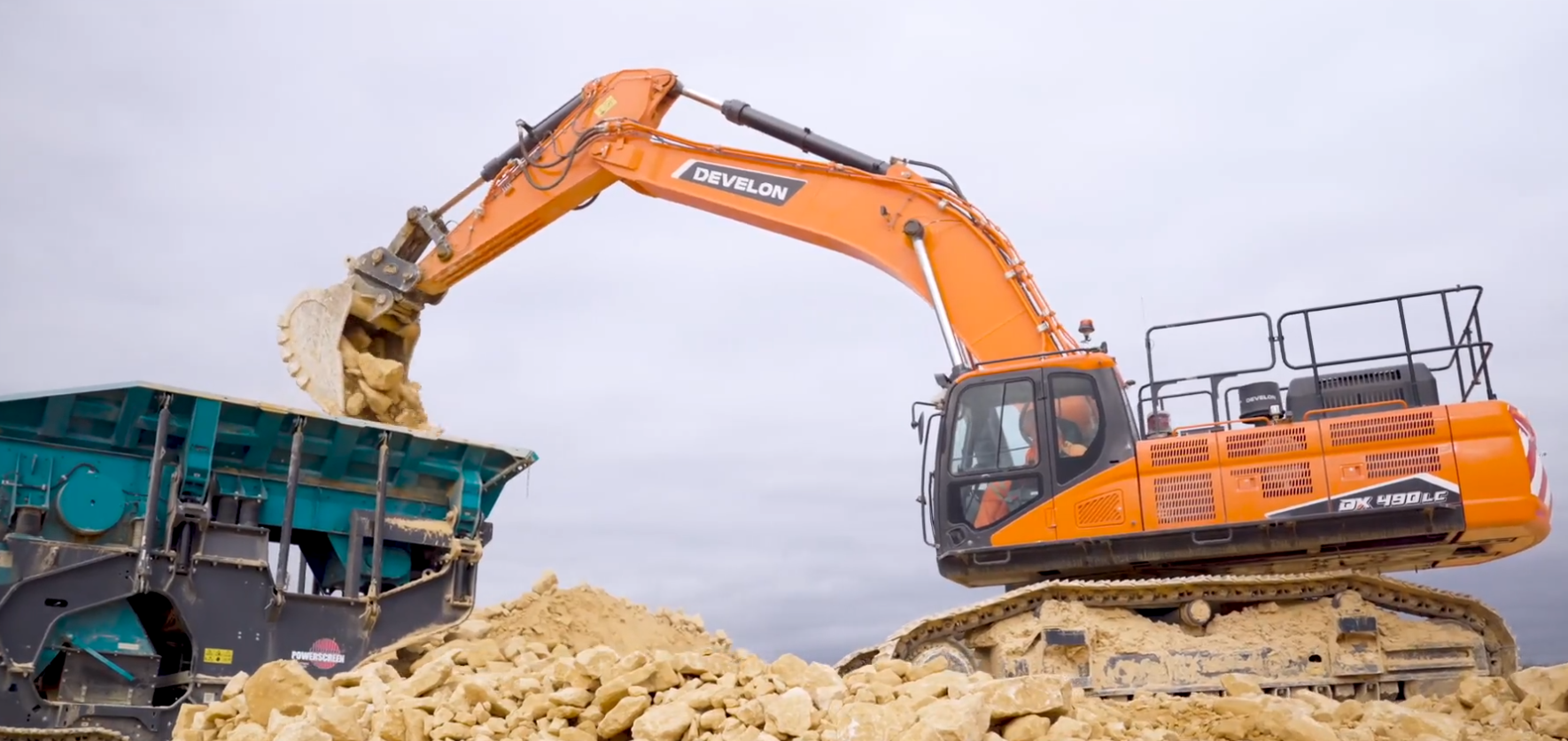 Orange Develon excavator loading quarried stone into a crusher