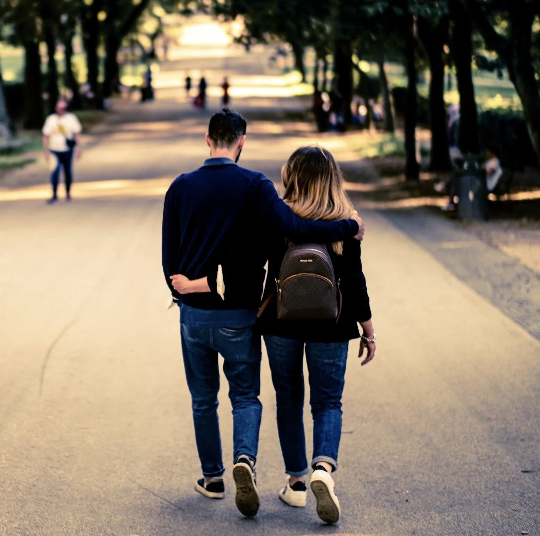A couple walking arm in arm down a tree-lined avenue