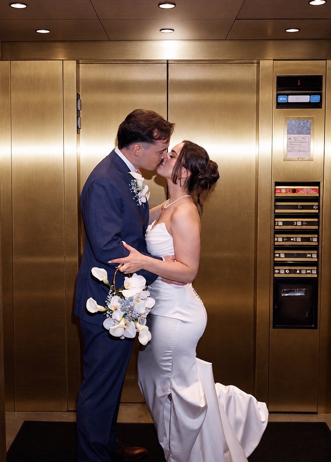 Rachel and her partner kissing in a gold elevator, with her orchid purse and his boutonniere.