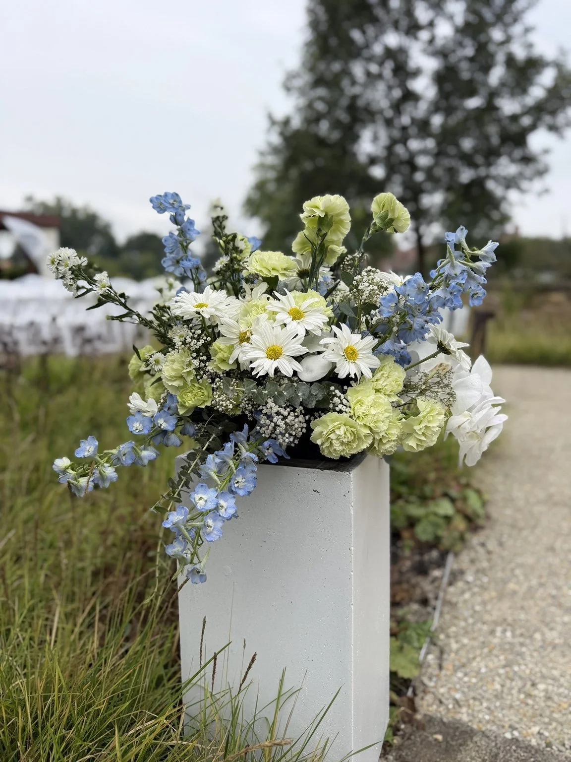 White, pale blue and green wedding flowers arranged on a white pedestal at Lake Ellyn.