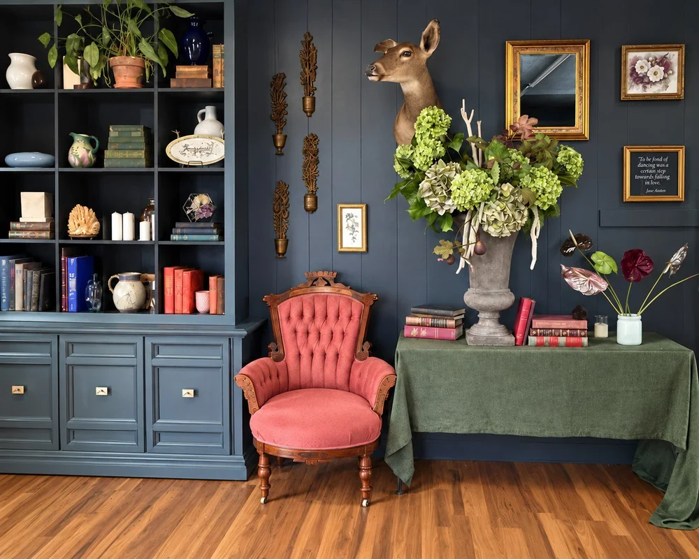 A corner of the Esotarium studio with vintage objects, a pink chair and flowers on a green-draped table.