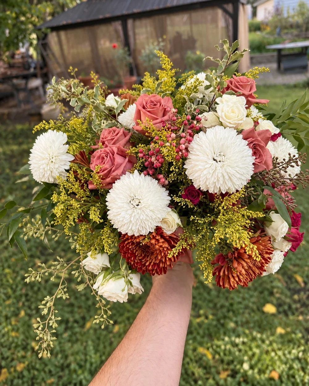 White chrysanthemums, dusty pink roses and rust flowers in a seasonal arrangement.
