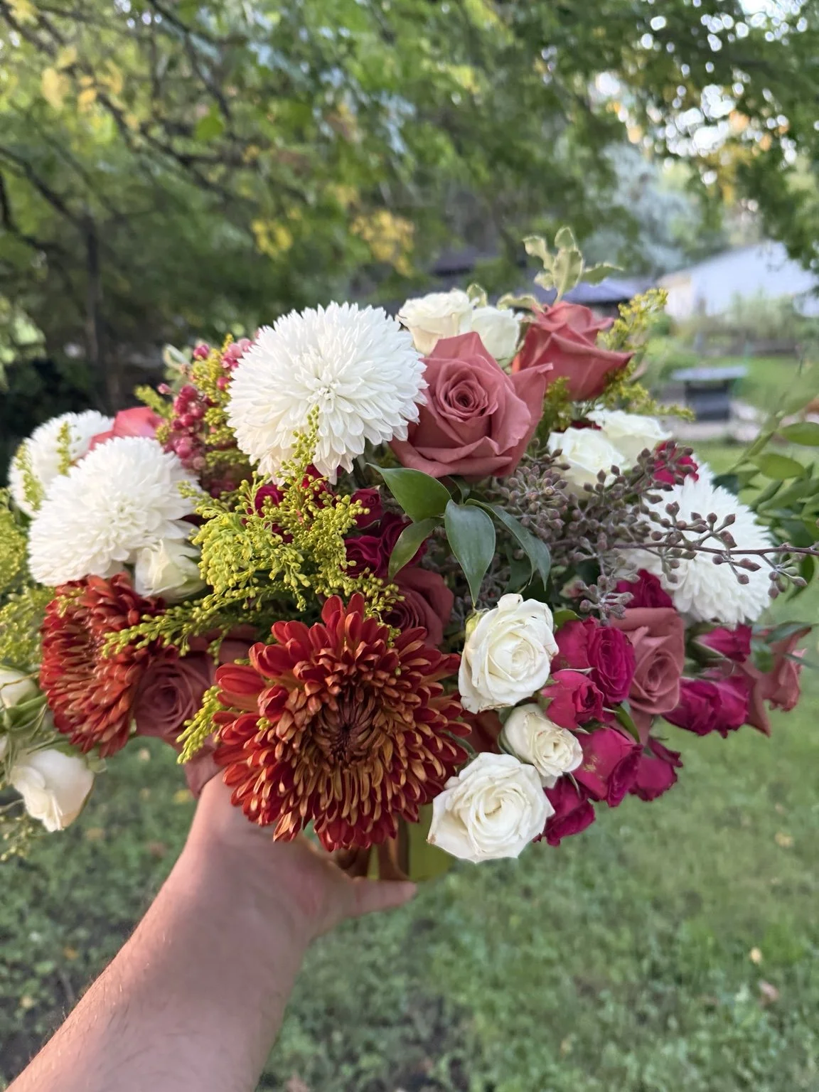 A seasonal arrangement of pink roses, white and rust chrysanthemums, and greenery in a gold vessel.