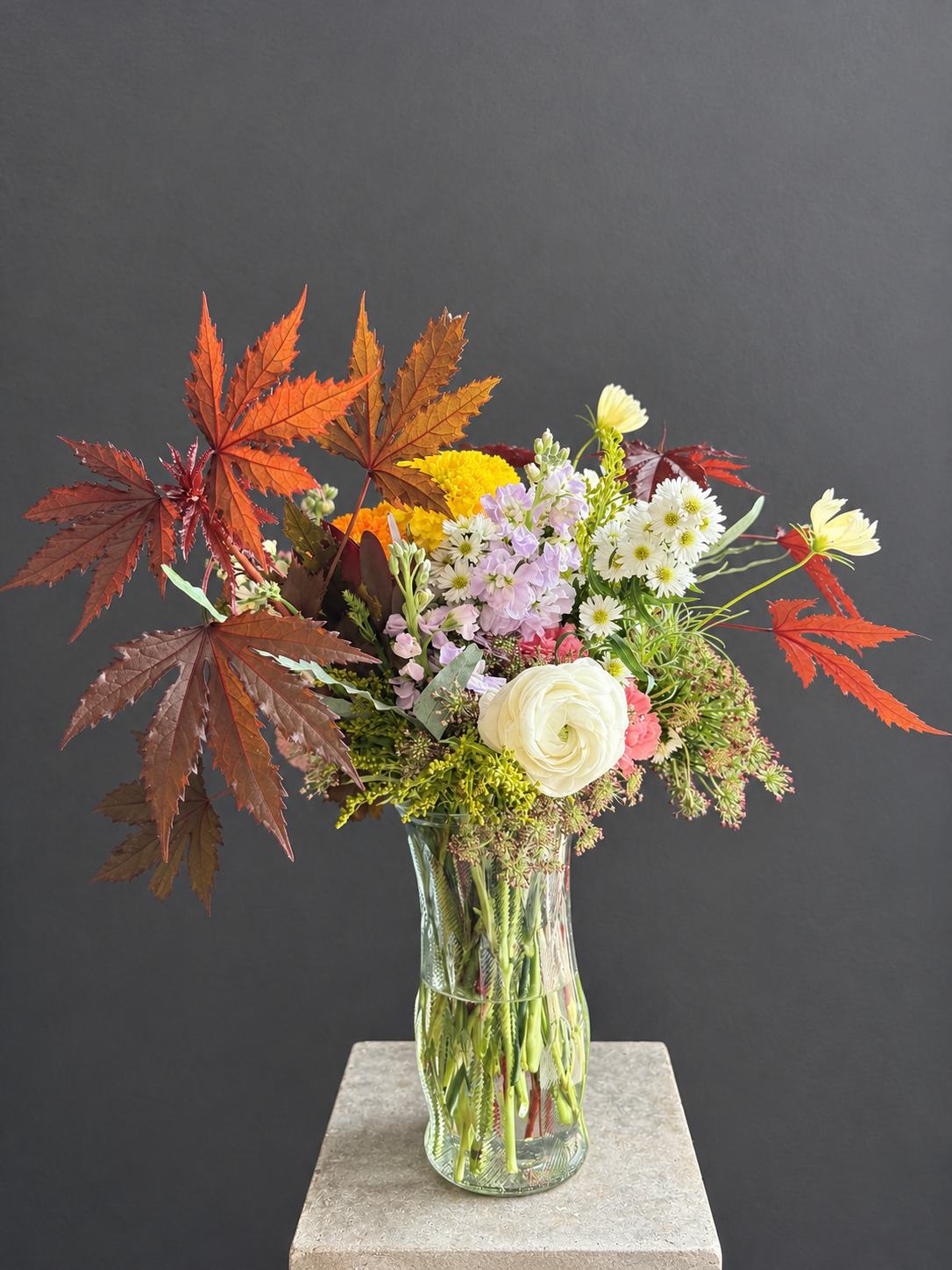 Seasonal Esotarium flowers in warm orange, pink and gold, arranged in a clear glass vase.