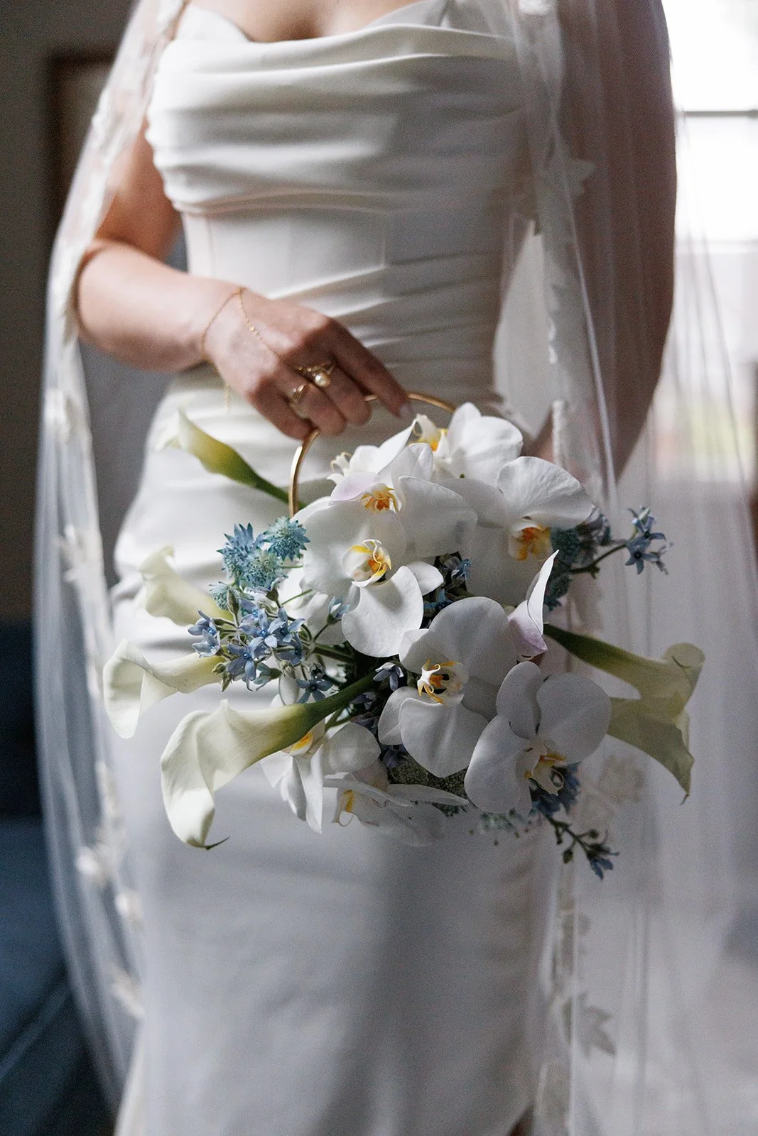 White orchids and calla lilies shaped into a floral purse with a gold handle, carried against Rachel’s wedding dress.
