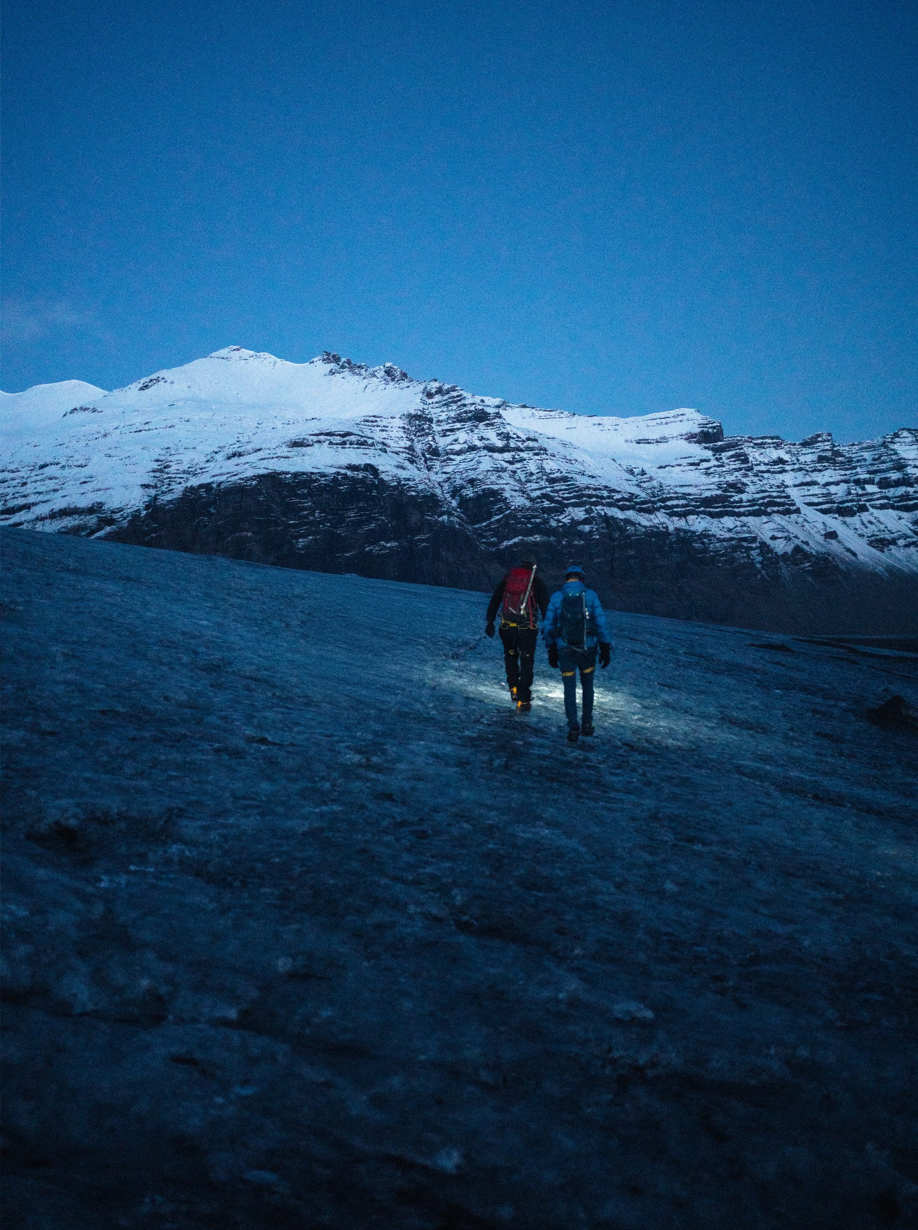 Dos montañeros avanzan por un paisaje nevado al amanecer