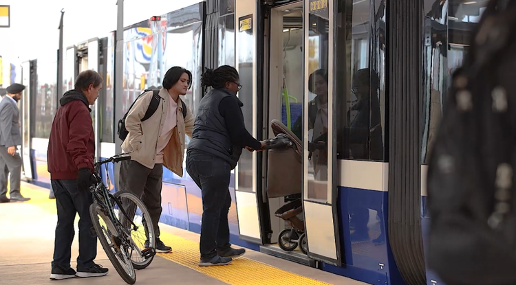 Riders step aboard an LRT vehicle from the platform, one with a bicycle