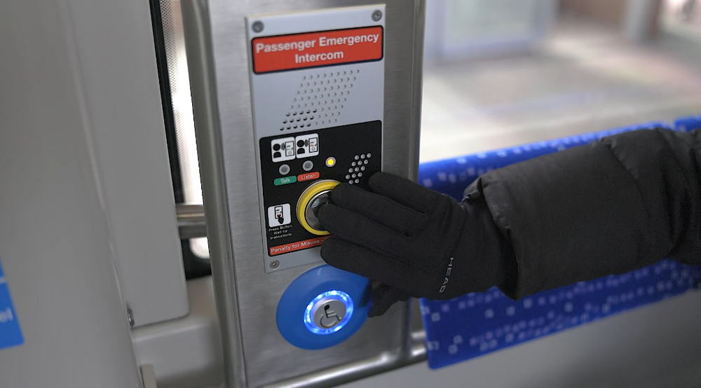 A gloved hand presses the passenger emergency intercom button inside an LRT vehicle