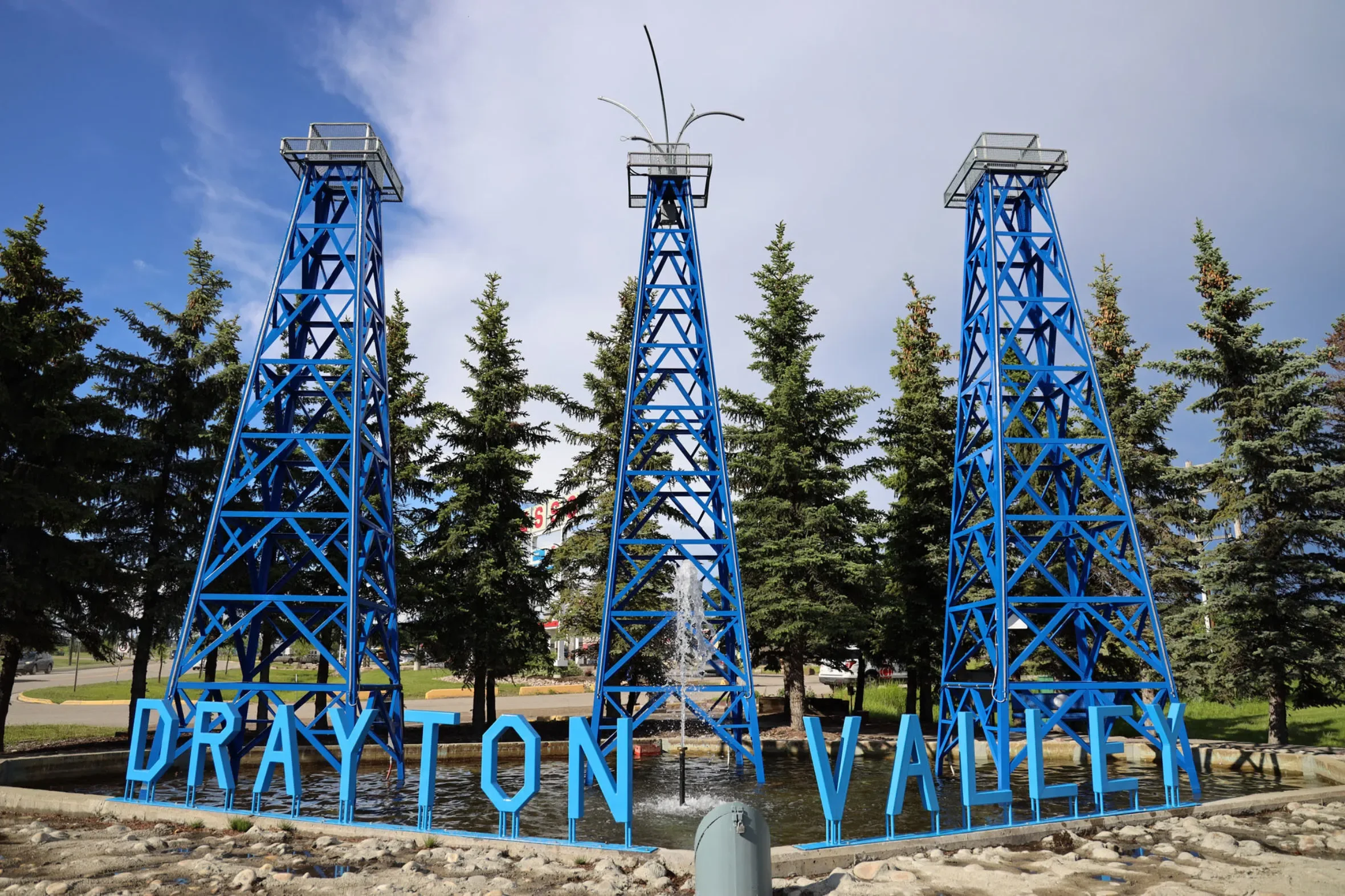 Blue oil derrick towers above the Drayton Valley sign