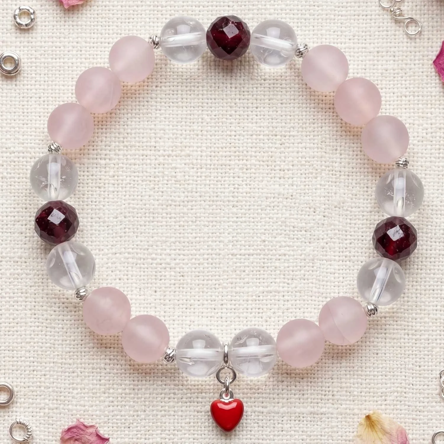 Edelsteinarmband mit Rosenquarz, Granat und Bergkristall mit Fenster sowie 925 Silber und Herzanhänger auf heller Oberfläche inszeniert