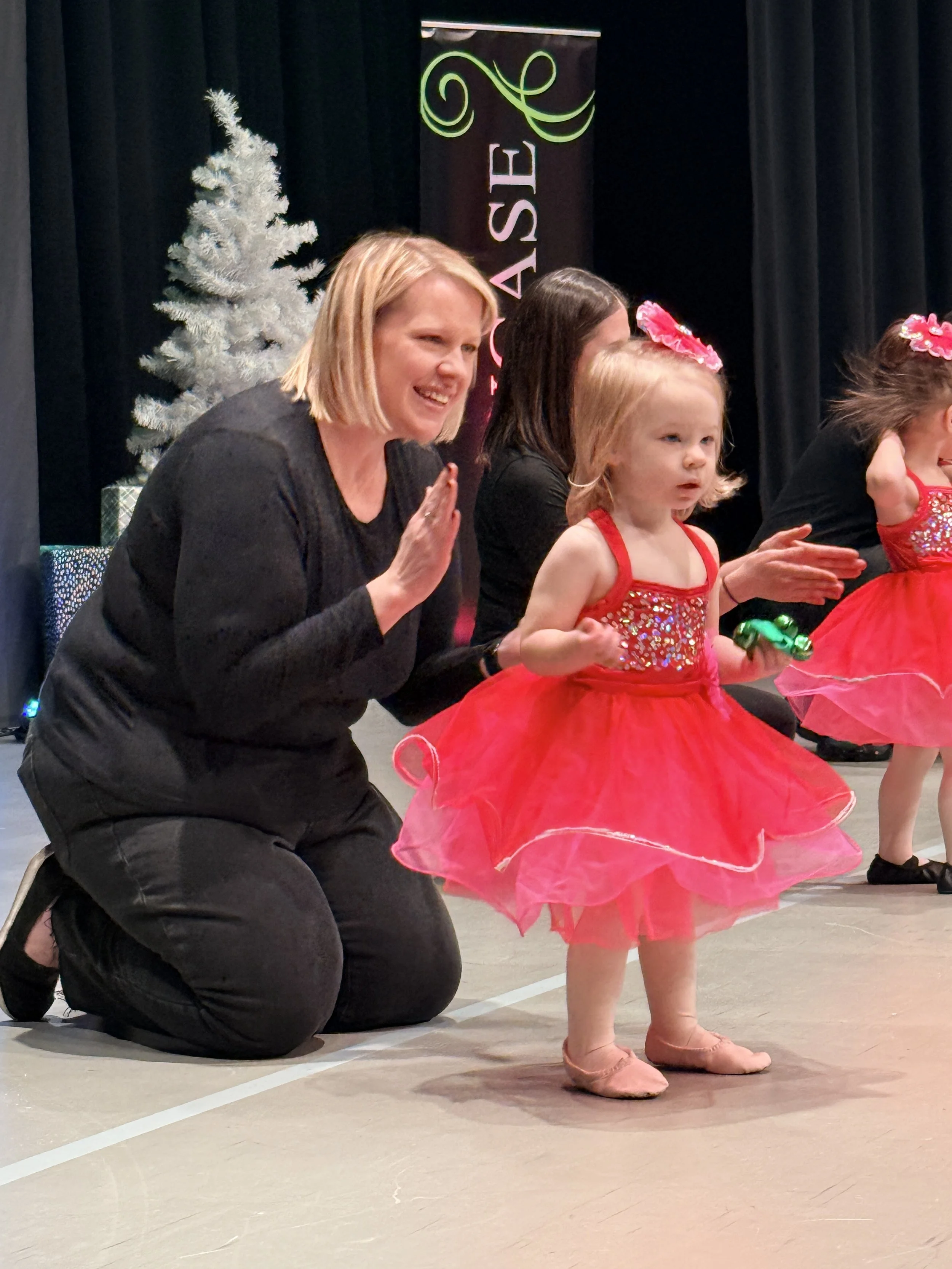 An AIM teacher kneeling beside a young dancer in a red costume during a holiday performance
