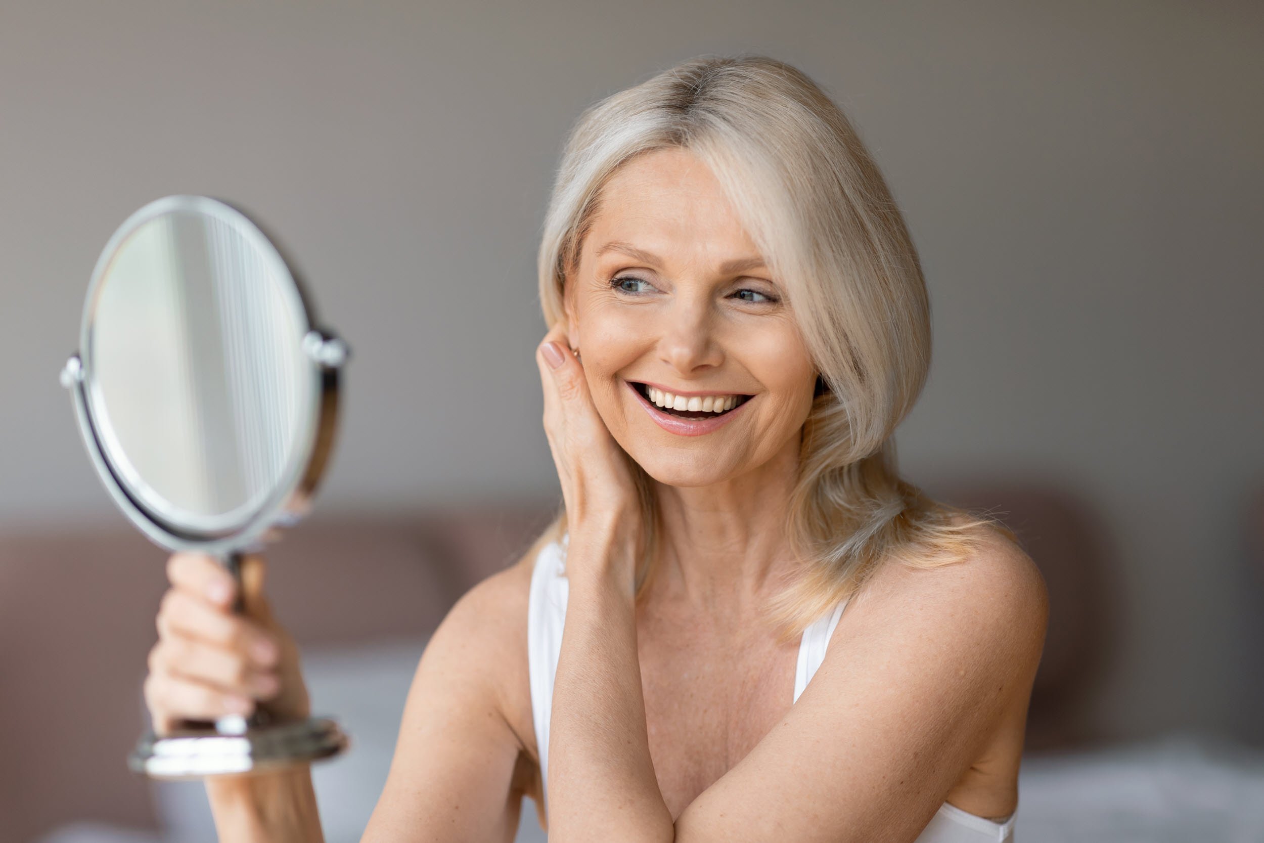 Smiling woman admiring her clear, radiant skin in a hand mirror