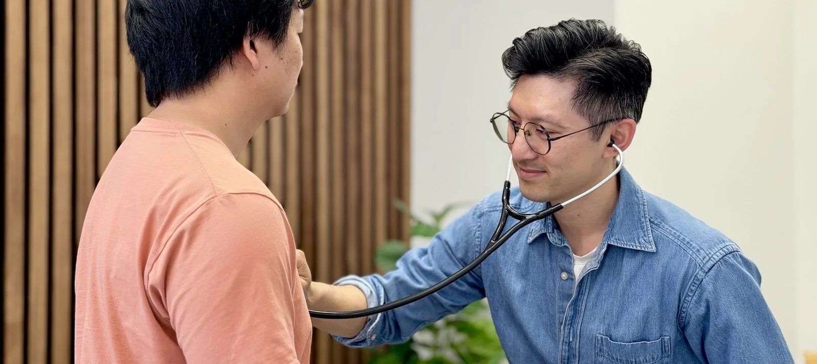 Dr. Siu smiles as he examines a patient with a stethoscope in Claremont, CA.