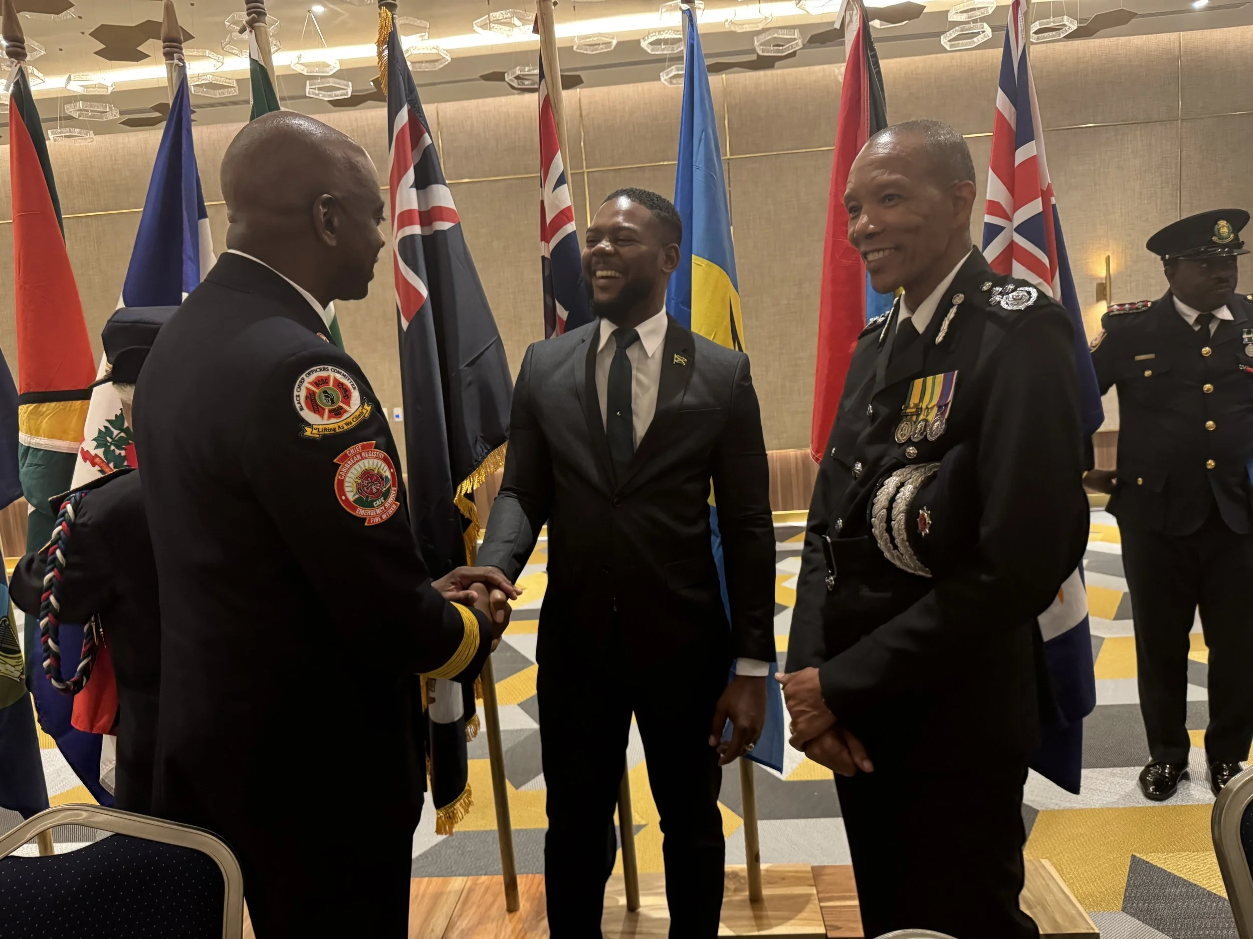 Caribbean fire chiefs networking at CAFC 2025 — Caribbean flags backdrop
