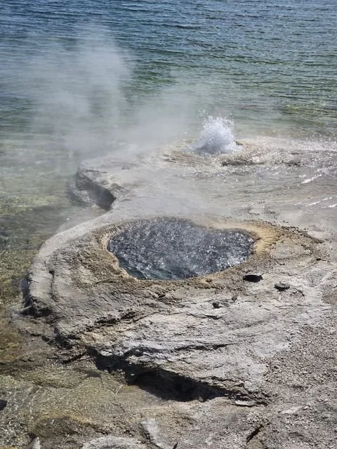 Steam and a small jet of water rise from Lakeshore Geyser beside Yellowstone Lake.