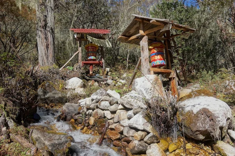 Water tumbles through the stones below the wooden prayer-wheel shelters.