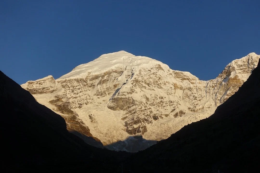 Golden light reaches the mountain’s snowy face while the valley remains in shadow.