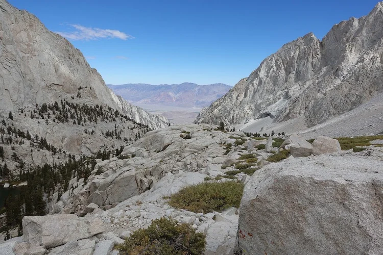 Scattered conifers return among the granite slabs as the view opens down the valley towards the dry lowlands.