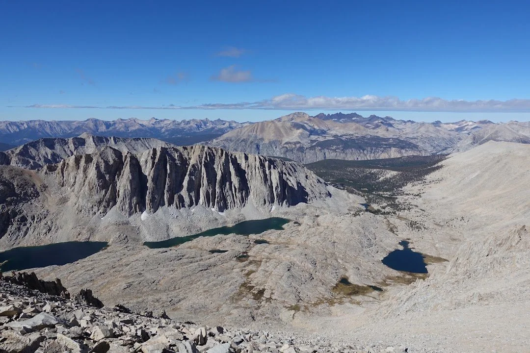 A chain of dark blue and turquoise lakes lies in the broad granite basin below the crest.