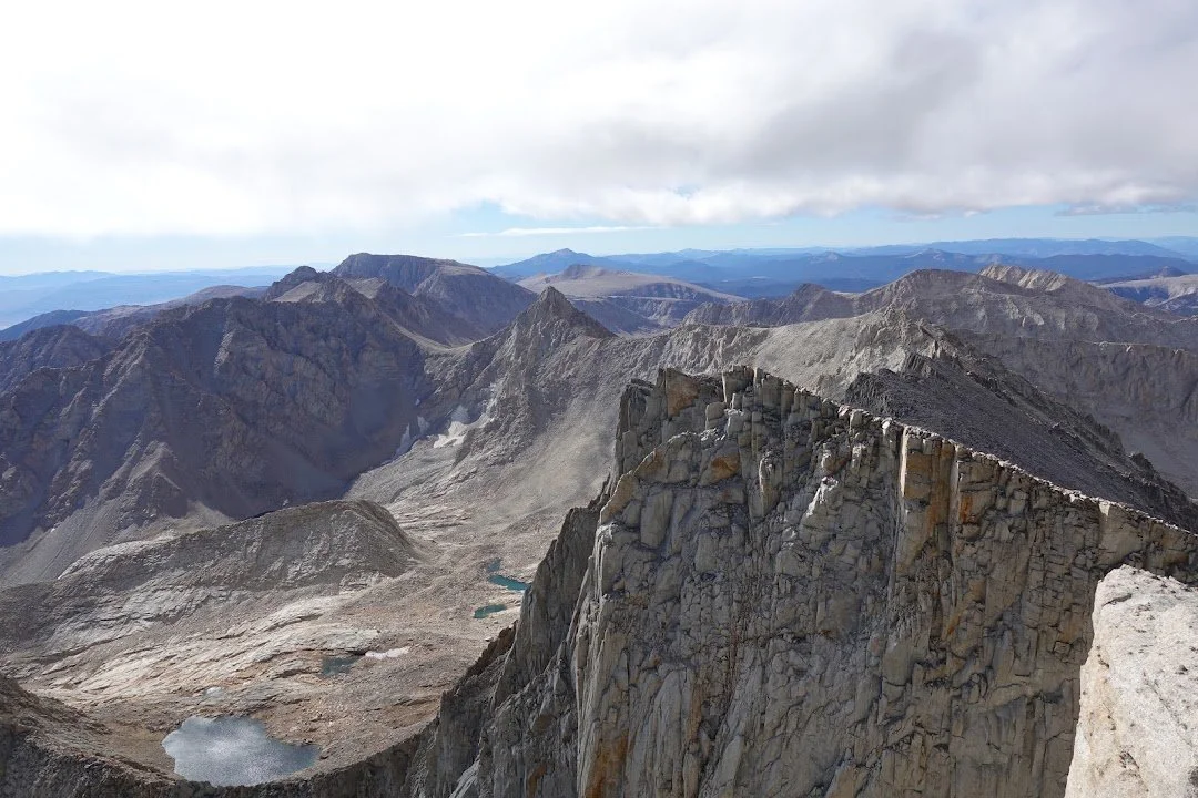 Small blue-green lakes punctuate the pale rocky basin below a towering granite cliff near the summit.