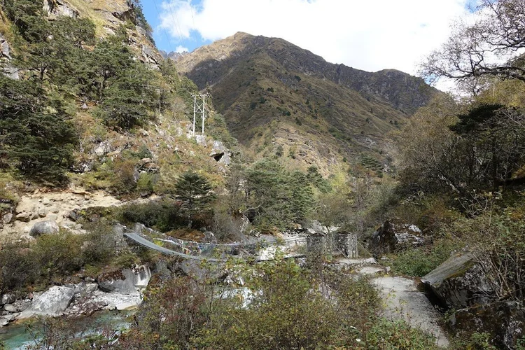 A narrow bridge carries the path across a rocky channel between steep slopes.