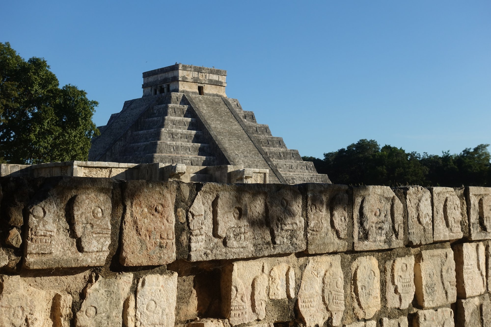 Rows of carved skulls cover the Tzompantli, with El Castillo rising behind it at Chichén Itzá.