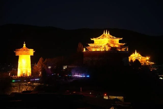 Golden light outlines temple roofs and a prayer wheel above the town.