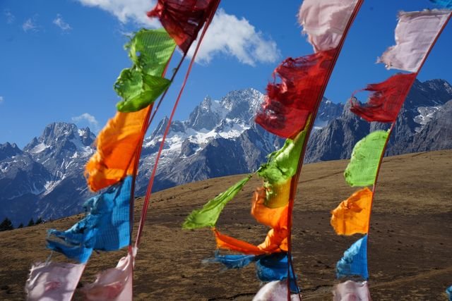 Prayer flags stream across a view of Yulong's snow-streaked peaks.