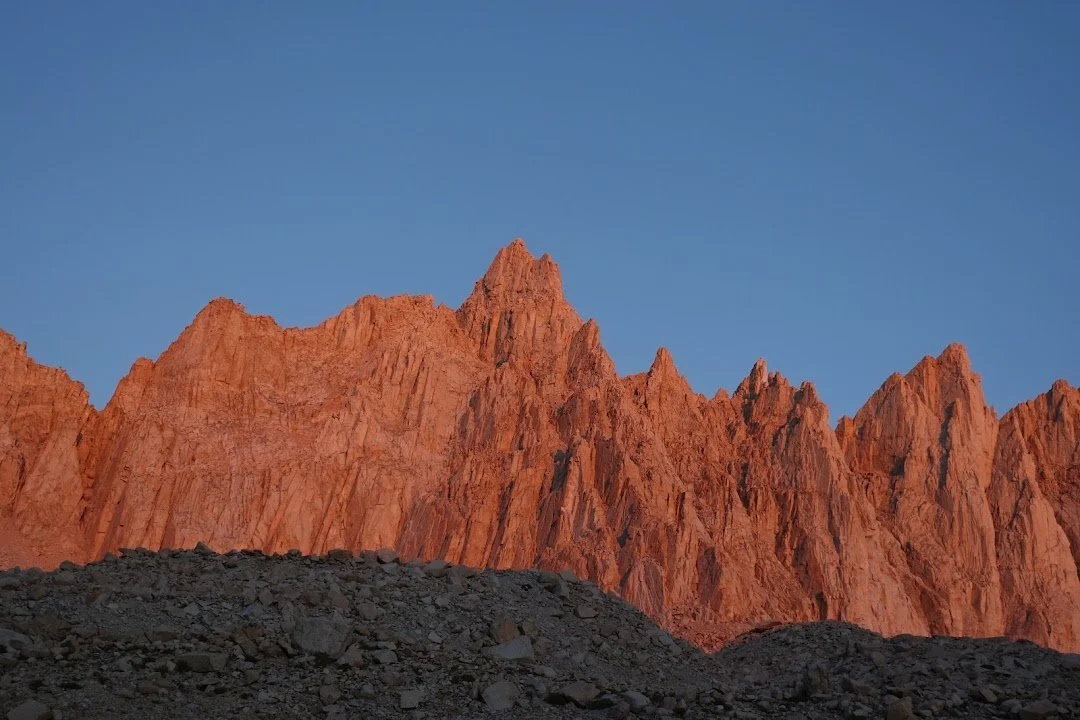 The rising sun turns the jagged granite spires a vivid orange above the still-shadowed scree.