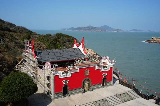 Curved rooflines and a red facade face the sea at Niufengjing Wulinggong Temple.