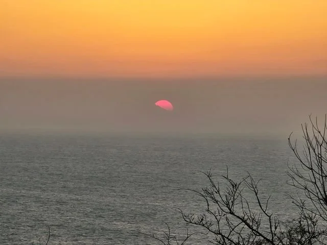 A pink sun hangs in the haze above the sea.