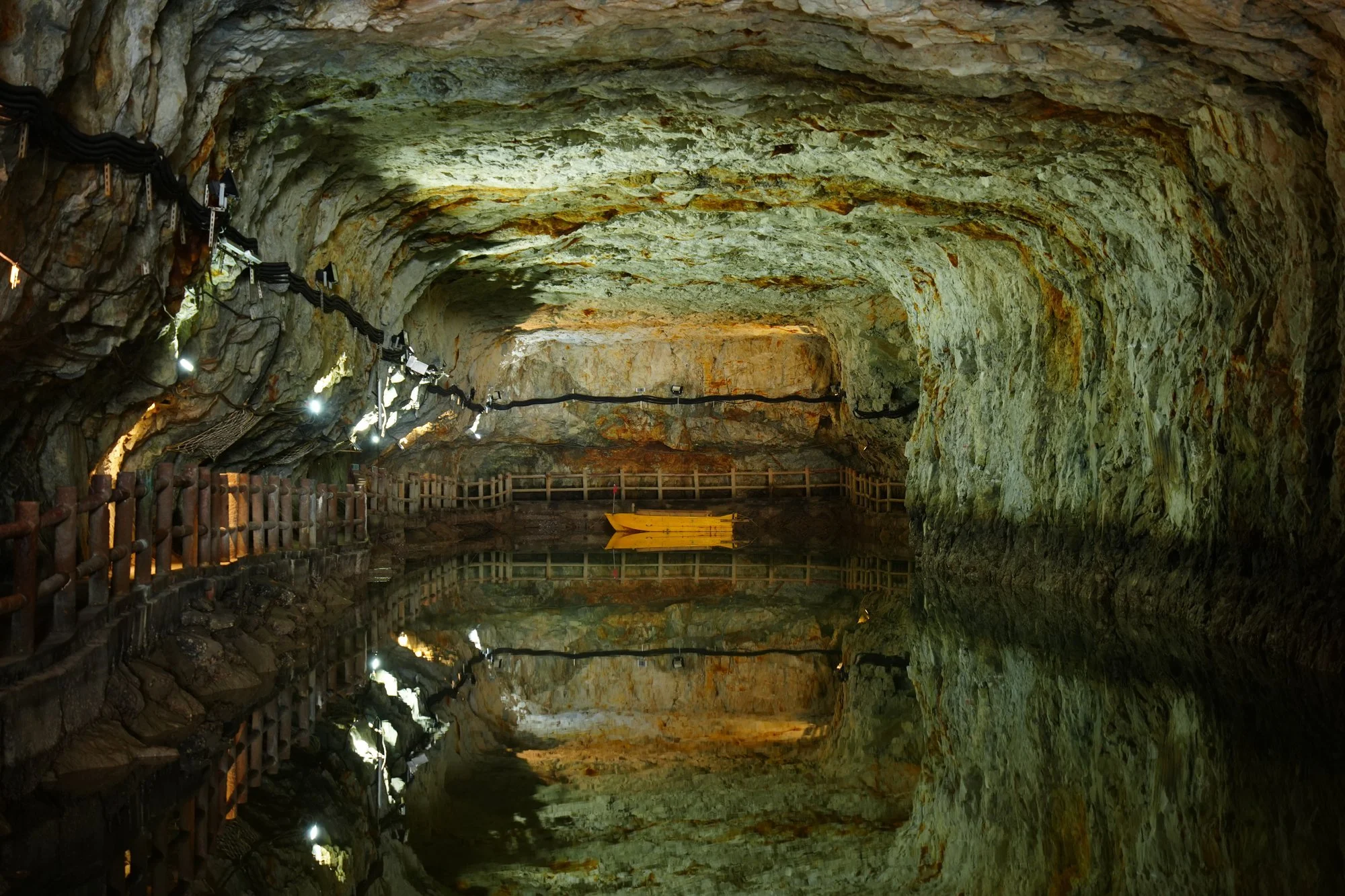 The rough stone arch of Beihai Tunnel is mirrored in still water beside an empty yellow boat.