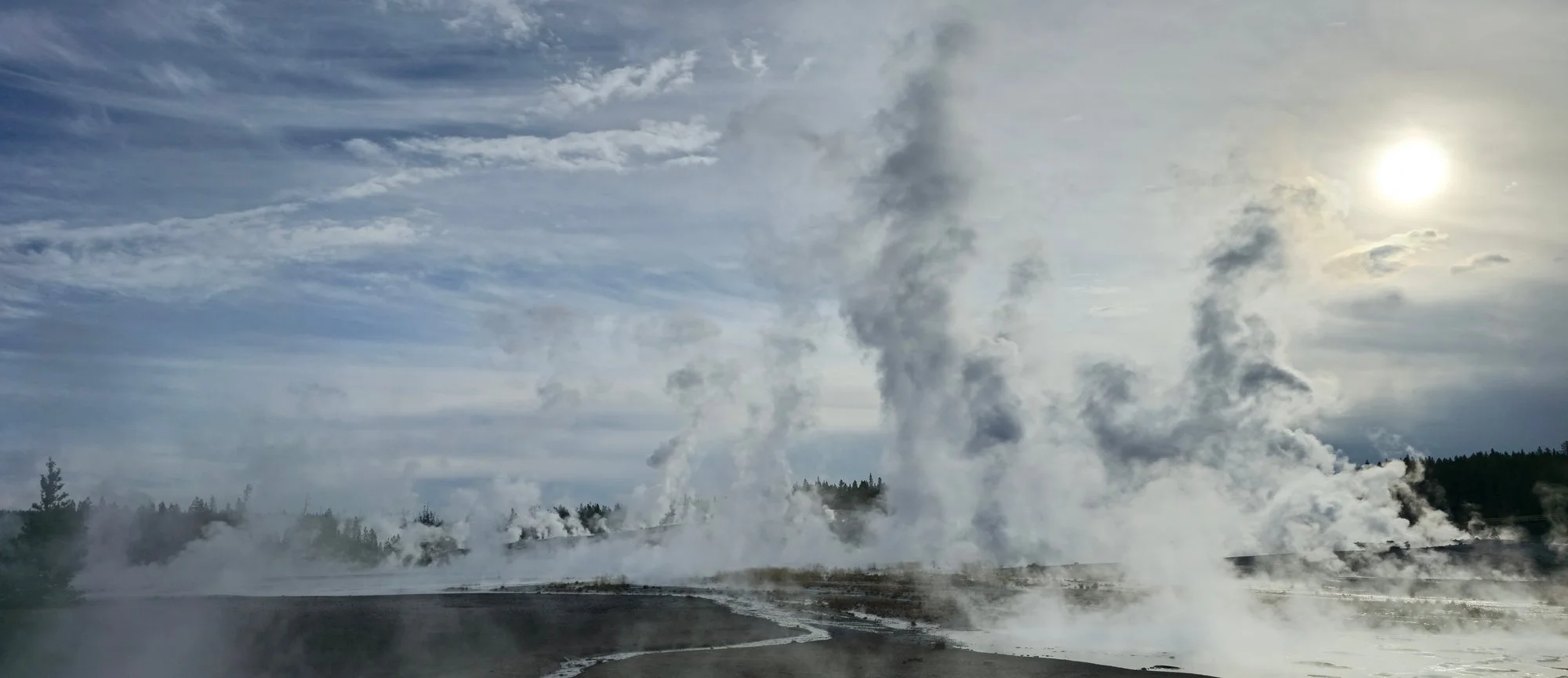 Low sunlight catches drifting steam above the dark mineral flats of Porcelain Basin.