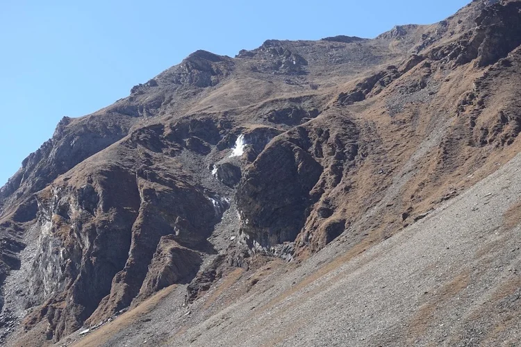 A small frozen cascade clings to the rock face above a wide slope of scree.