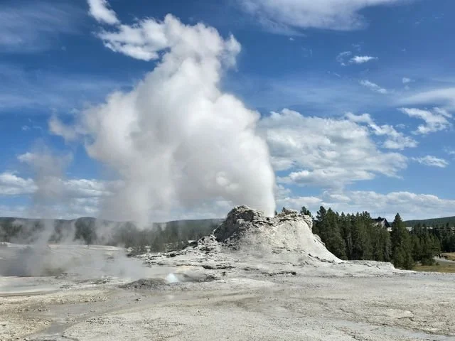A white plume rises above the massive, irregular cone of Castle Geyser.