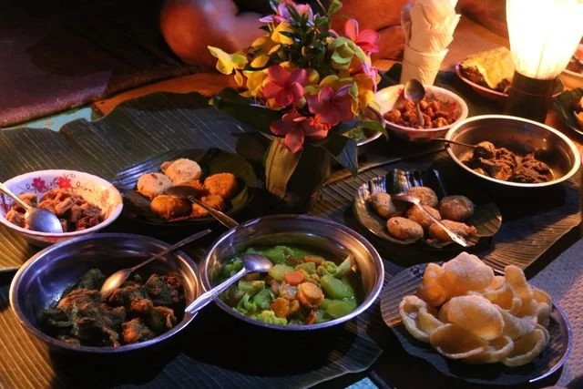 Dinner is laid out on leaves and metal dishes beneath a warm camp light.
