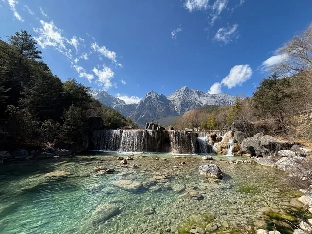 Clear water runs over broad stone steps, with the mountain ridge beyond.