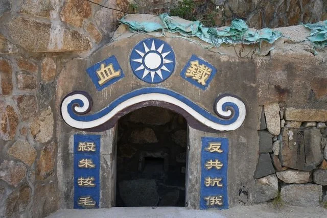 Painted slogans and a white sun emblem frame an old military doorway on Nangan.