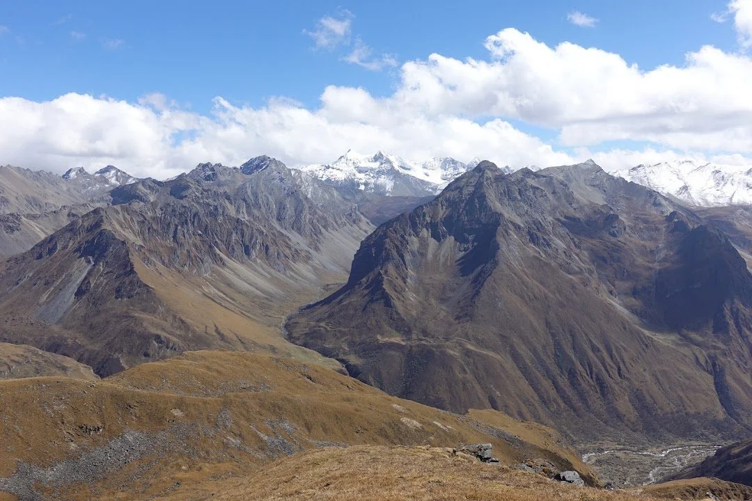 Brown ridges fold into deep valleys, with snowy summits rising beyond them.