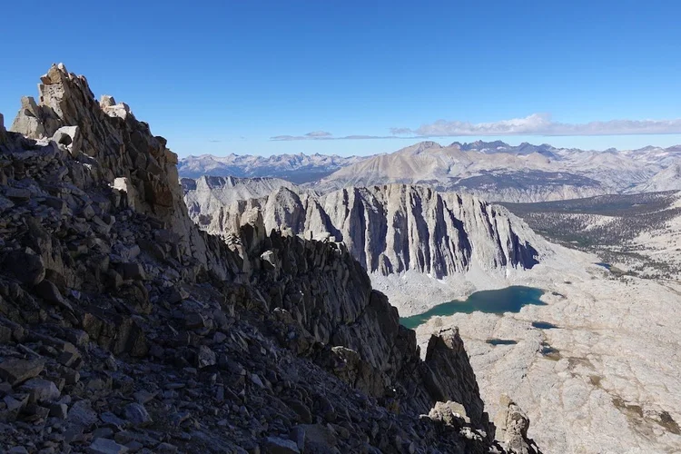 The shaded rock towers beside the trail open onto sunlit cliffs and a long turquoise lake far below.