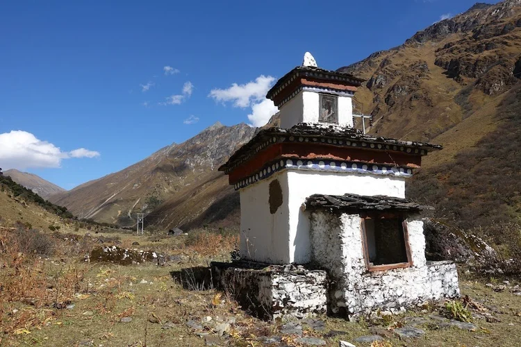 A weathered chorten stands beside the trail, its white walls bright against the brown mountains.