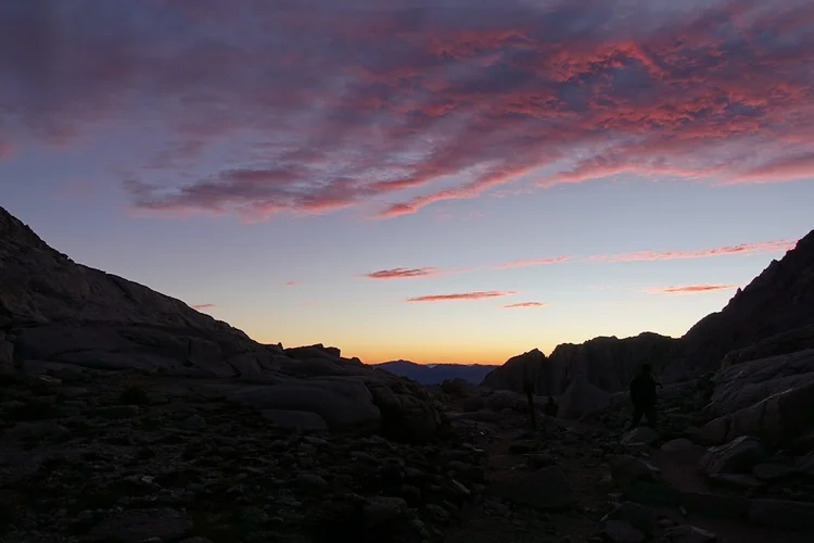 Pink and orange clouds brighten the sky above the dark, rocky basin.