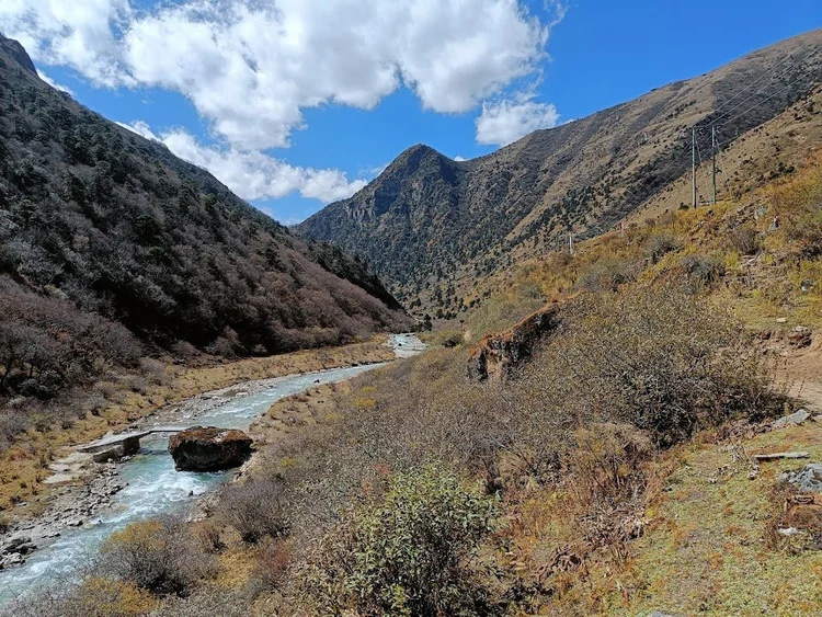 The pale blue river winds between autumn shrubs and steep valley walls.