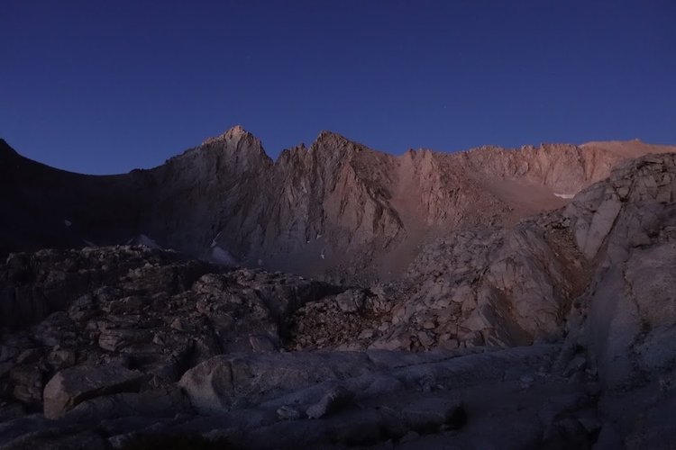The first pale light reveals jagged granite walls above a foreground of shattered rock.