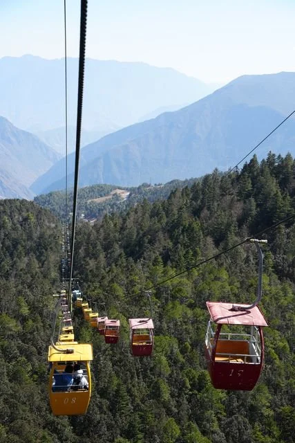 Yellow and red cable cars hang above the forested slopes.