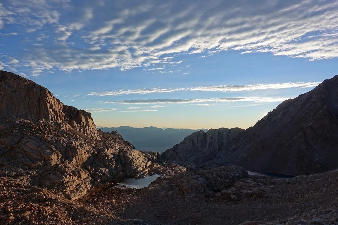 Two alpine lakes lie among the bare granite ridges, beneath streaks of morning cloud.