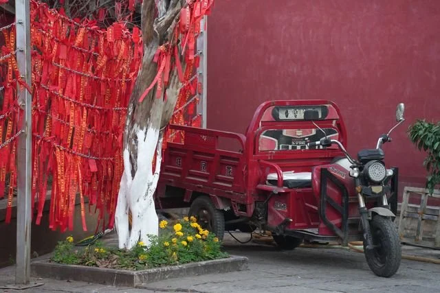 A red cargo tricycle sits beside a tree hung with red ribbons.